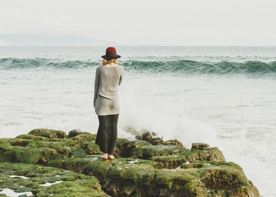 女人站在绿色岩石与波附近的水域
